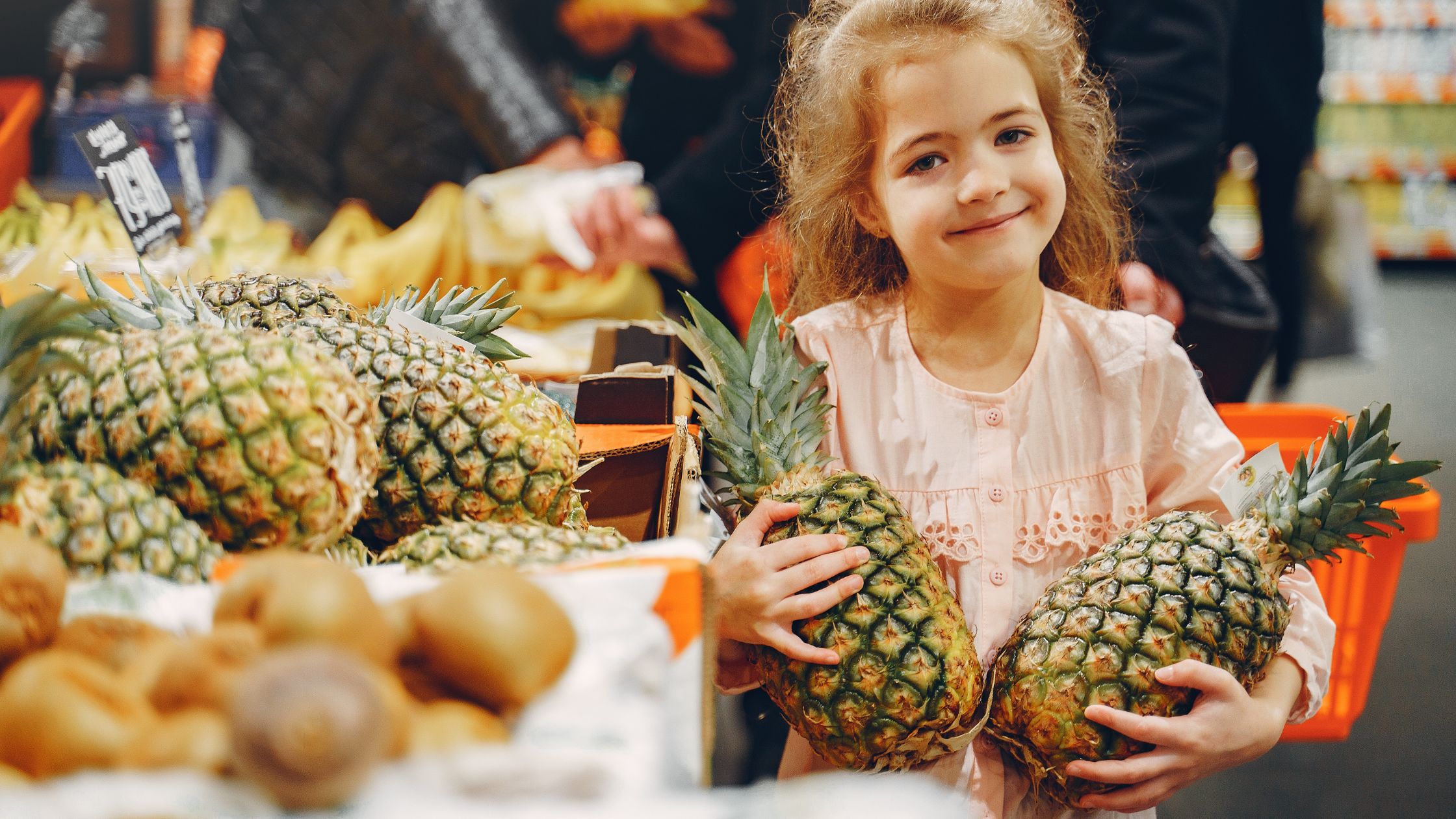 A young girl carrying two pineapples on sale