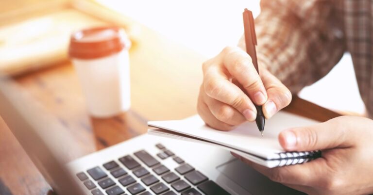 Writing in a notebook with a laptop on table